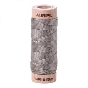 Puede incluir: Una bobina de hilo Aurifil de color gris claro. La bobina es de madera y tiene el logotipo de Aurifil impreso en ella. El texto "Made in Italy" está impreso en la parte inferior de la bobina.