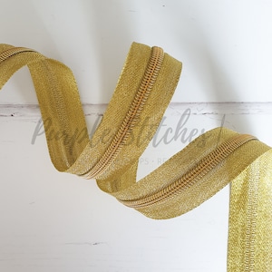 Op de afbeelding: Gouden ritsband met een metallic afwerking. Het ritsband is opgerold en heeft een subtiel herringbone-patroon.