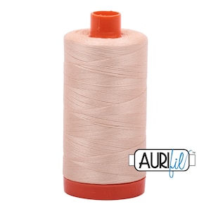 Puede incluir: Un carrete de hilo color melocotón claro con tapa y base naranja. El hilo está bien enrollado y la marca "AURIfil" está impresa en el lateral. Adecuado para proyectos de costura y acolchado.