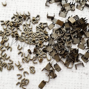 Op de afbeelding: Een grote hoeveelheid antieke gouden metalen ritsen. De ritsen zijn U-vormig en vierkant.