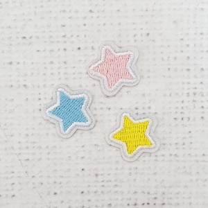May include: Three embroidered felt star patches in pink, blue, and yellow. The stars are outlined in white.