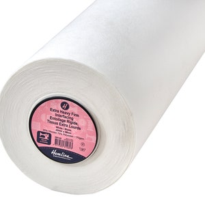 Puede incluir: Un rollo grande de entretela blanca extra firme. La etiqueta circular en el extremo presenta el texto: Extra Heavy Firm Interfacing, 30% Viscosa 70% Poliéster, 170gsm, 25m x 96cm, y el logotipo de la marca Hemline con iconos de costura.