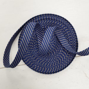 Peut inclure: Une bobine de ruban bleu marine avec de fines rayures dorées. Le ruban est enroulé serré, mettant en valeur le motif et la texture du tissu. Les rayures diagonales créent un design visuellement attrayant.