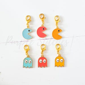Op de afbeelding: Zes kleurrijke Pac-Man- en spookbedels met goudkleurige sluitingen. De Pac-Man-bedels zijn blauw, rood en oranje. De spookbedels zijn blauw, rood en geel. Perfect voor een sleutelhanger of ketting.
