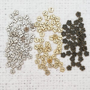 May include: A collection of small, decorative metal flower-shaped beads in silver, gold, and bronze.