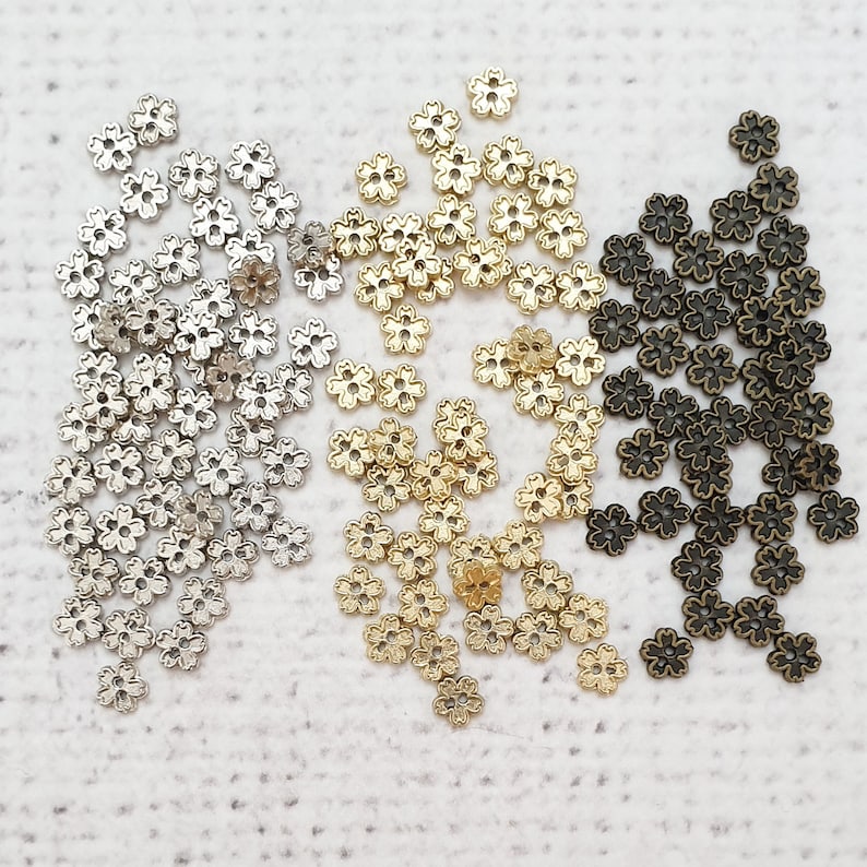 May include: A collection of small, decorative metal flower-shaped beads in silver, gold, and bronze.
