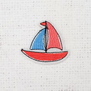 Puede incluir: Un parche bordado de un velero rojo y azul. El velero está bordeado de negro y tiene una vela blanca.