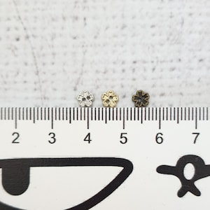 May include: Three small metal flower-shaped charms in silver, gold, and black, measured against a ruler.
