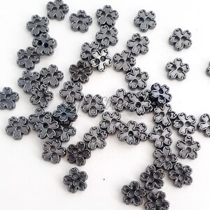 May include: A large quantity of small, black metal flower-shaped buttons. The buttons have a shiny, slightly metallic finish.