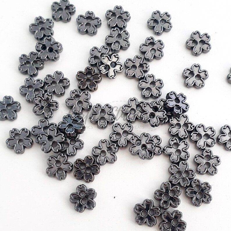 May include: A large quantity of small, black metal flower-shaped buttons. The buttons have a shiny, slightly metallic finish.