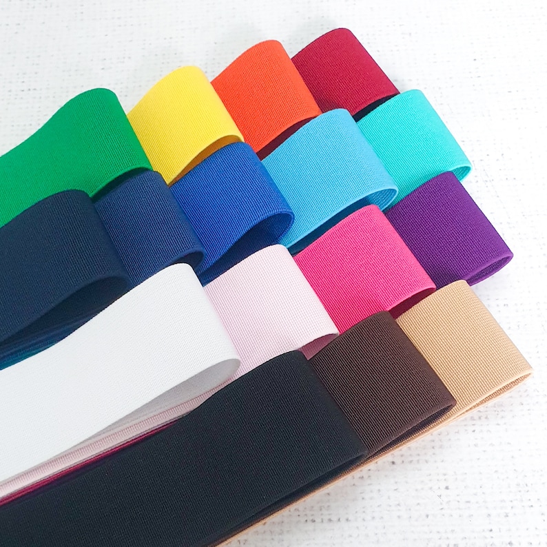 Pu&ograve; includere: Una collezione di 12 diversi colori di bordino elastico in tessuto. Il bordino &egrave; disposto a ventaglio, con i colori pi&ugrave; scuri in basso e i colori pi&ugrave; chiari in alto. I colori includono nero, marrone, beige, rosa, viola, turchese, blu, giallo, arancione, rosso e verde.