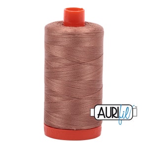 Pode incluir: Um carretel de linha Aurifil na cor rosa suave. A linha é enrolada firmemente em torno de um núcleo cilíndrico, coberto por uma tampa laranja brilhante. O logotipo da Aurifil é visível na lateral.