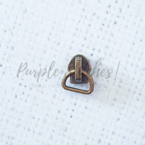 May include: A gold-toned metal zipper pull with a D-ring. The zipper pull is designed to be used with a zipper on a garment or bag.