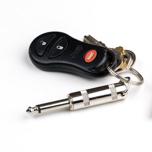May include: A black Jeep car key fob with a red panic button attached to a silver key chain with a silver 1/4 inch guitar cable.