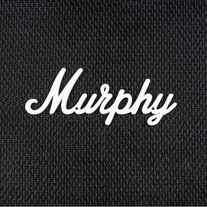 May include: White cursive text on a black fabric background that reads "Murphy".