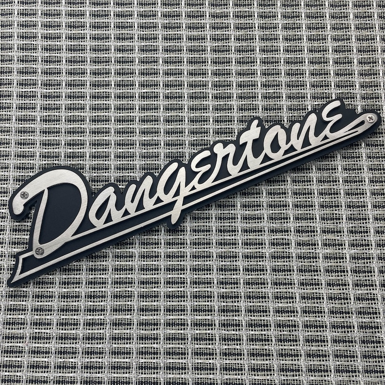 May include: A black metal logo with the word "Dangerstone" in a stylized font. The logo is attached to a silver speaker grill.