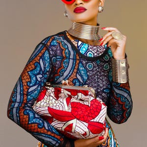 May include: A woman wearing a colourful patterned dress with a black mesh overlay, red cat-eye sunglasses, and a silver choker necklace. She is holding a red and white patterned clutch purse.
