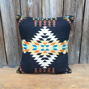 May include: A black throw pillow with a geometric pattern in shades of orange, yellow, blue, and white. The pattern is reminiscent of Native American designs.