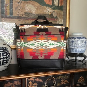 May include: A black leather backpack with a brown and red patterned fabric front. The backpack is sitting on a black lacquered table with gold accents and Chinese characters.