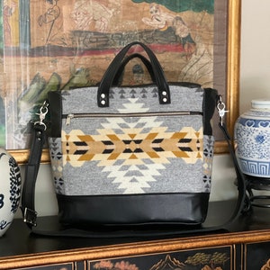 May include: A black and gray tote bag with a geometric pattern and a black leather bottom. The bag has a top handle and a long shoulder strap.