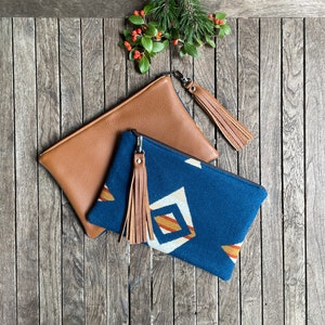 May include: Two clutches, one brown leather and one blue with a geometric pattern, both with brown leather tassels.