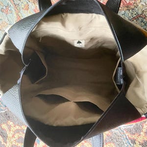 Puede incluir: El interior de un bolso tote de cuero negro con un forro de tela marr&oacute;n. El bolso tiene un cierre de cremallera y un peque&ntilde;o bolsillo en el interior.