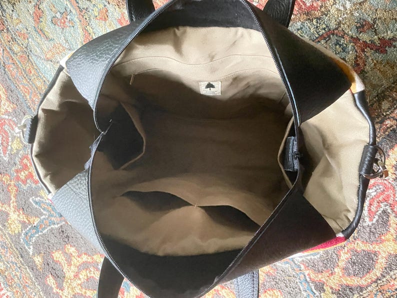 Puede incluir: El interior de un bolso tote de cuero negro con un forro de tela marr&oacute;n. El bolso tiene un cierre de cremallera y un peque&ntilde;o bolsillo en el interior.