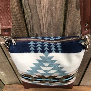 May include: A blue and white patterned crossbody bag with a brown leather strap and bottom. The bag has a zipper closure and a geometric design.