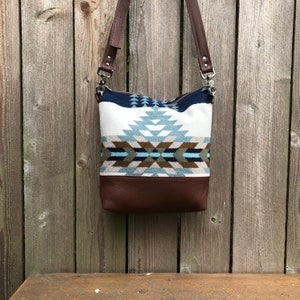 May include: A brown leather and woven fabric shoulder bag with a geometric pattern in shades of blue, white, and brown.