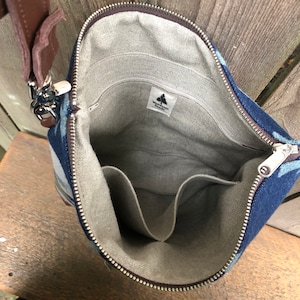 May include: Inside view of a blue and white patterned canvas bag with a zipper closure. The bag has a brown leather strap and a gray fabric lining with multiple pockets. The bag has a label that reads "Woodside Goods".
