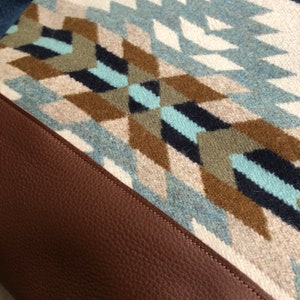 May include: A brown leather bag with a geometric patterned fabric flap. The fabric is a mix of blue, white, brown, and black.