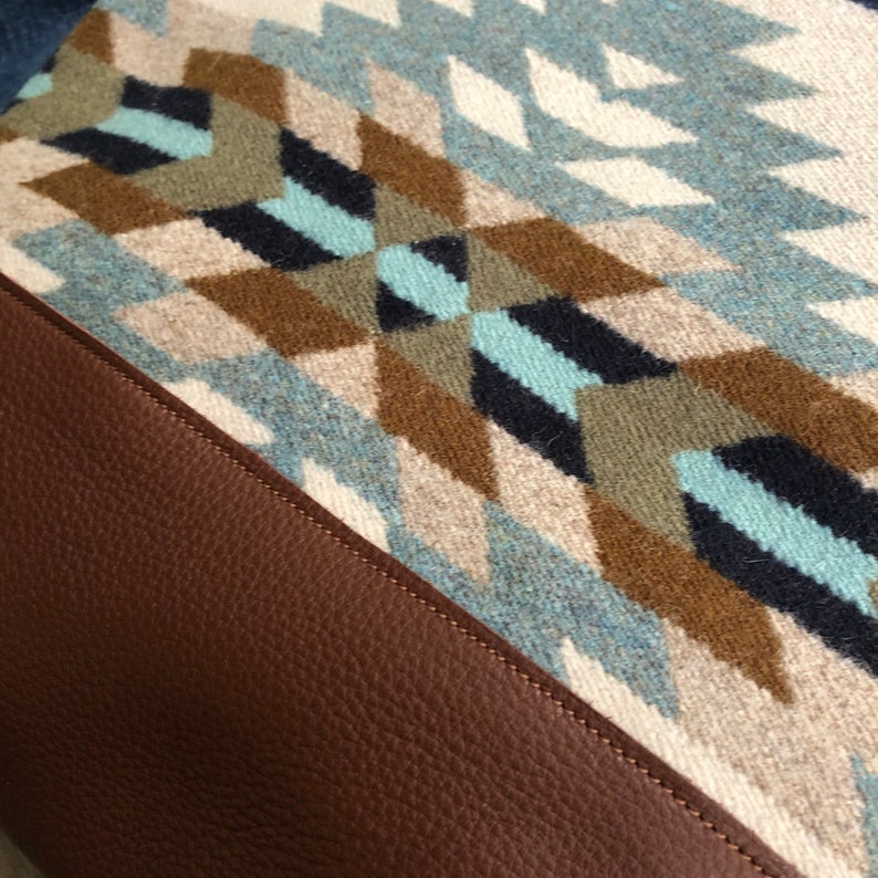 May include: A brown leather bag with a geometric patterned fabric flap. The fabric is a mix of blue, white, brown, and black.
