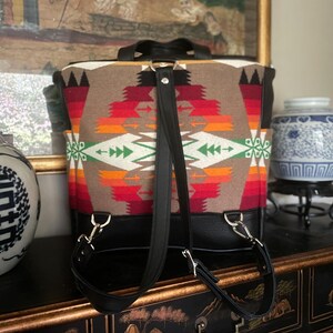 Puede incluir: Una mochila de cuero negro con correas ajustables. La mochila est&aacute; hecha de una tela tejida con un patr&oacute;n geom&eacute;trico colorido.