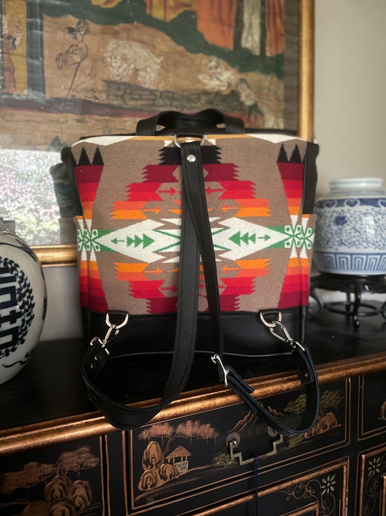 Puede incluir: Una mochila de cuero negro con correas ajustables. La mochila est&aacute; hecha de una tela tejida con un patr&oacute;n geom&eacute;trico colorido.