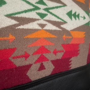 Puede incluir: Primer plano de una tela con estampado rojo, naranja, verde y blanco con ribete de cuero negro. La tela tiene un dise&ntilde;o geom&eacute;trico con flechas y tri&aacute;ngulos.