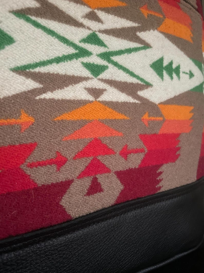 Puede incluir: Primer plano de una tela con estampado rojo, naranja, verde y blanco con ribete de cuero negro. La tela tiene un dise&ntilde;o geom&eacute;trico con flechas y tri&aacute;ngulos.