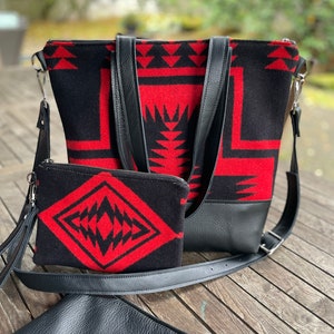 K&ouml;nnte beinhalten: Eine schwarze und rote geometrisch gemusterte Tragetasche mit einer passenden kleineren Tasche und einem schwarzen Leder-Umh&auml;ngegurt.