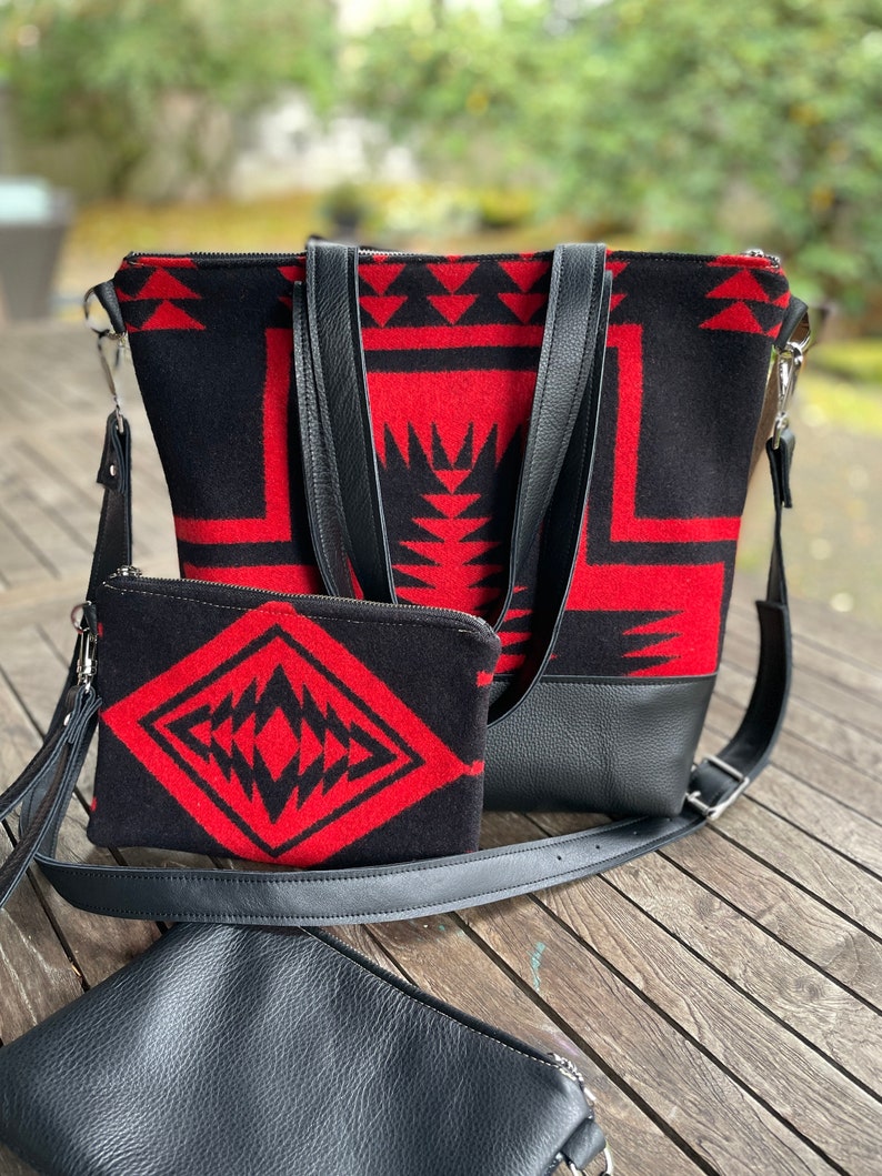 K&ouml;nnte beinhalten: Eine schwarze und rote geometrisch gemusterte Tragetasche mit einer passenden kleineren Tasche und einem schwarzen Leder-Umh&auml;ngegurt.