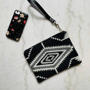 May include: Black and white geometric patterned clutch with a black leather wrist strap and a silver clasp.