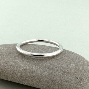 May include: A simple silver band ring, resting on a gray stone.
