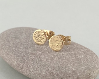 May include: A pair of gold hammered circle stud earrings. The earrings are small and delicate, and they have a textured surface.