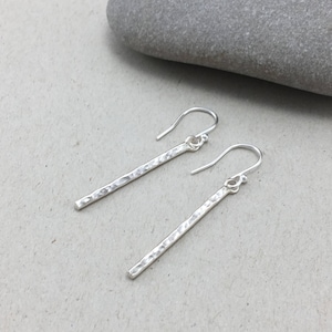 May include: A pair of silver hammered bar earrings with a simple hook closure.