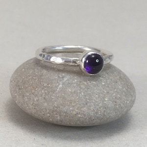 May include: A silver ring with a hammered texture and a small, round, purple amethyst gemstone.