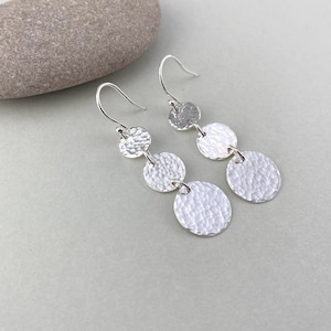 May include: Silver dangle earrings with three hammered circular discs on each earring.