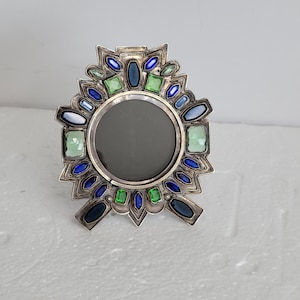 Pode incluir: Um porta-retratos de prata com um design de estrela. A moldura é decorada com pedras preciosas azuis, verdes e transparentes.