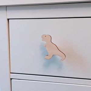 May include: White chest of drawers with a wooden dinosaur-shaped pull handle.