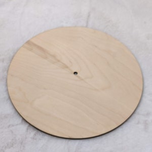 May include: A round, unfinished wooden craft blank with a natural wood grain. The blank has a small hole drilled near the center. This versatile craft supply is ideal for various DIY projects, including signs and home decor.