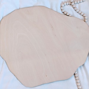 May include: A light brown, irregularly shaped wooden serving tray with a smooth surface. The tray is on a white fabric background.