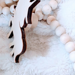 May include: A wooden unicorn cutout with a brown wood grain finish. The unicorn is standing on a white fluffy surface.