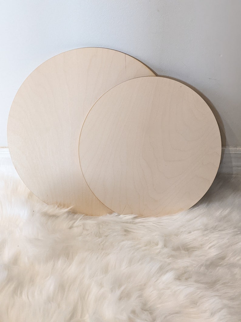May include: Two unfinished wooden circles, one larger than the other, on a white fluffy surface.